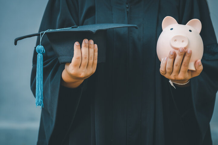 Graduate with cap and piggy bank in hands
